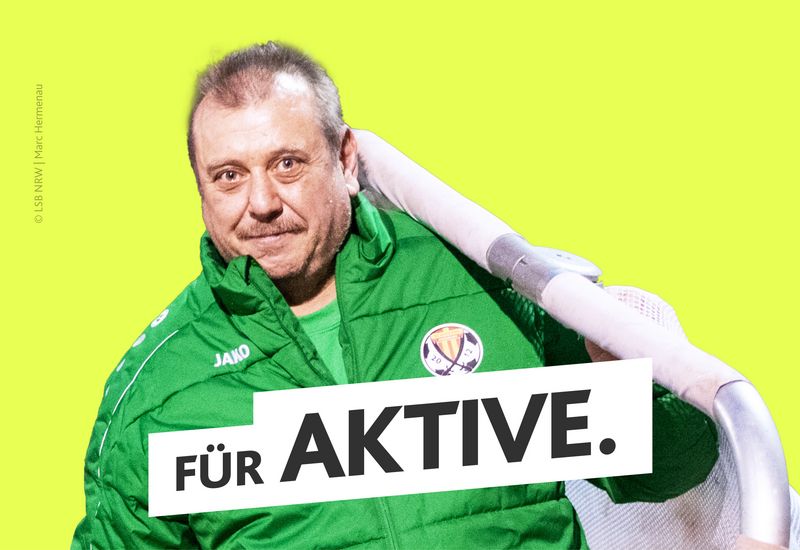 Mann in grüner Vereinsjacke hält ein Hockeytor. Er steht vor einer gelben Farbfläche.Text: ‚Für Aktive.‘