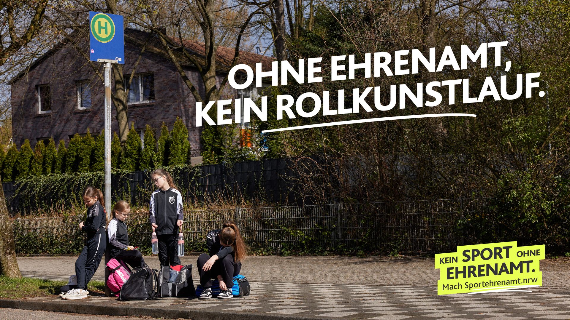 Eine Jugendmannschaft sitzt und steht mit Sporttaschen an einer Bushaltestelle und wartet auf die Fahrgelegenheit zum Training. Darüber steht „Ohne Ehrenamt, kein Rollkunstlauf“. Motiv Elterntaxi der LSB NRW Offensive 2026 mit dem Claim „Kein Sport ohne Ehrenamt. Mach Sportehrenamt.nrw“.