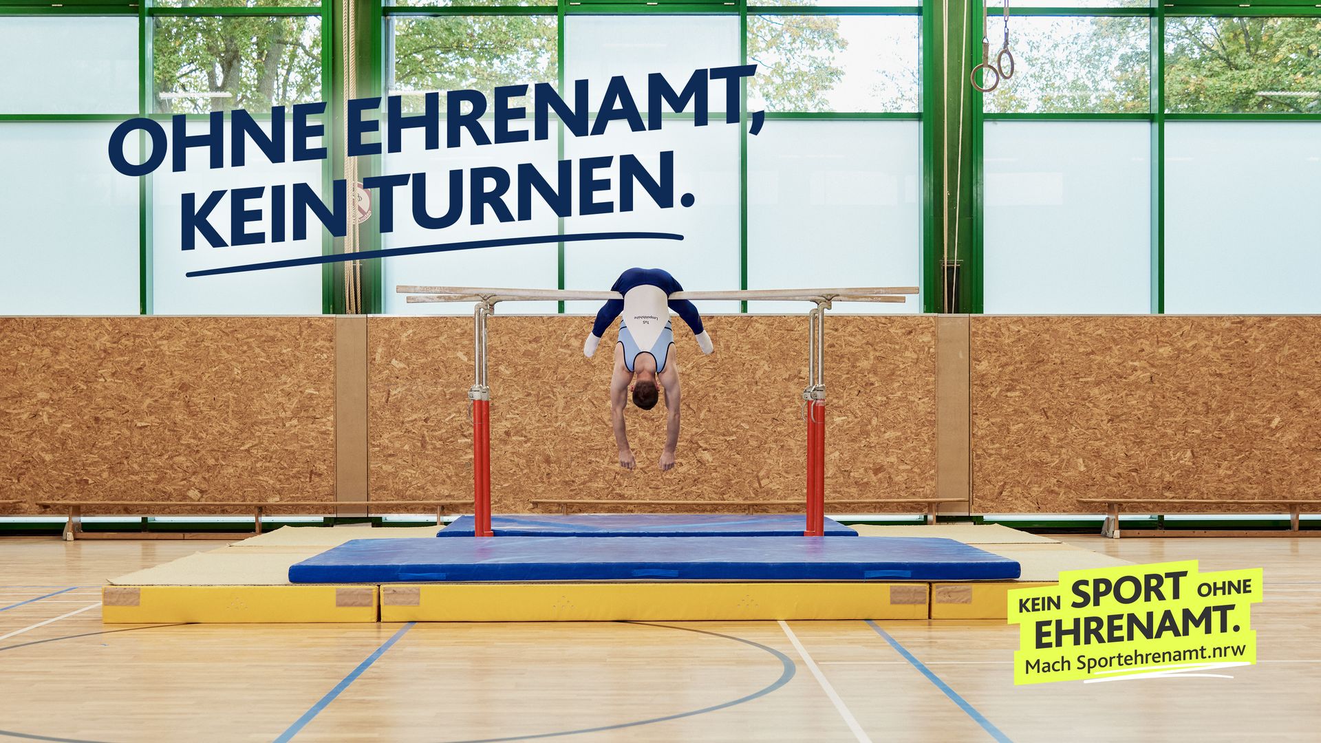 Turner hängt kopfüber mit baumelnden Armen am Barren. Darüber in dunkelblauer Schrift: „Ohne Ehrenamt, kein Turnen.” Motiv der LSB NRW-Offensive 2026: ‚Kein Sport ohne Ehrenamt.‘ Darunter der Aufruf ‚Mach Sportehrenamt.nrw‘.