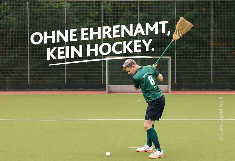 Hockeyspieler versucht mit einem Besen einen Ball zu schlagen. Darüber in weißer Schrift: „Ohne Ehrenamt, kein Hockey.” Motiv der LSB NRW Offensive 2026 zum Sportehrenamt mit dem Claim „Kein Sport ohne Ehrenamt“ und dem Aufruf „Mach Sportehrenamt.nrw“.