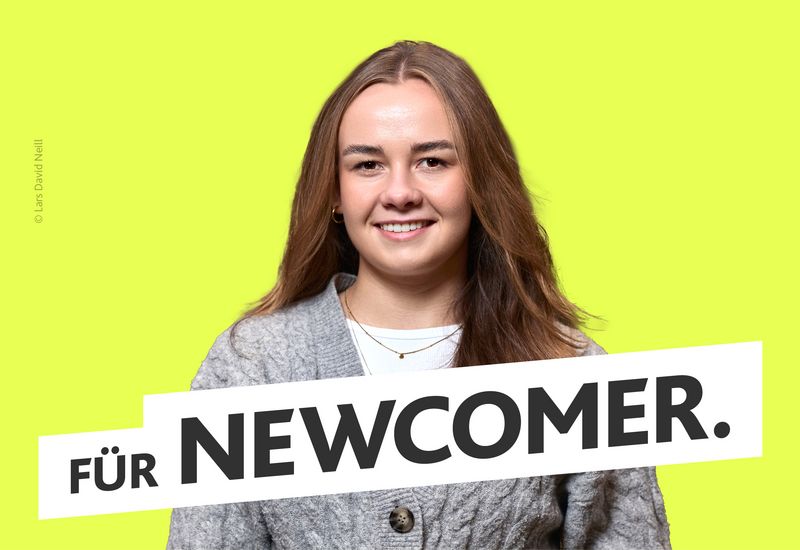 Junge Frau in grauer Strickjacke vor gelben Hintergrund. Text: ‚Für Newcomer.‘