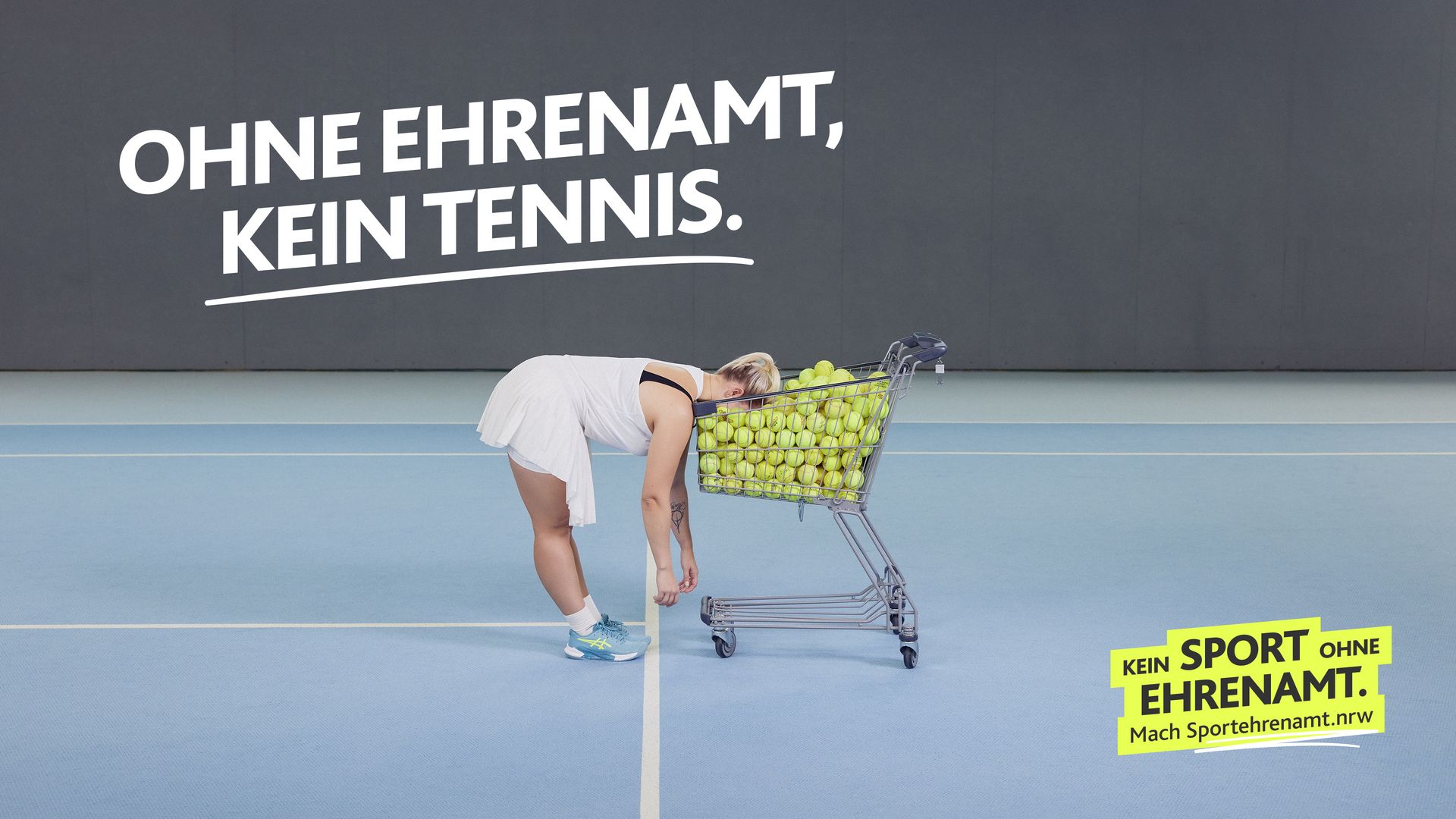 Tennisspielerin lehnt mit dem Kopf in einem Einkaufswagen voller Tennisbälle. Darüber in weißer Schrift: „Ohne Ehrenamt, kein Tennis. Motiv Tennis der LSB NRW-Offensive 2026: ‚Kein Sport ohne Ehrenamt. Mach Sportehrenamt.nrw‘.