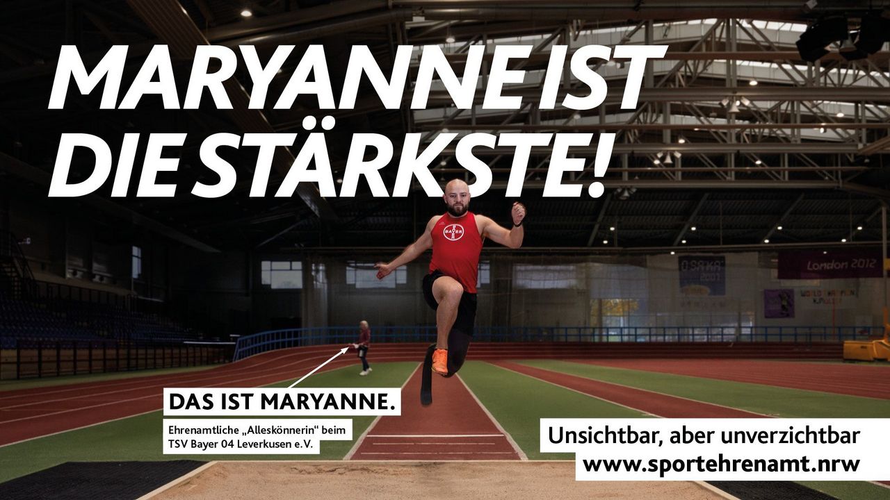 Ein Para-Leichtathlet beim Weitsprung in der Halle. Im Hintergrund überreicht die Ehrenamtliche des TSV Bayer 04 Leverkusen, Maryanne, einen Picknickkorb zur Stärkung. Aufdruck: ‚Maryanne ist die Stärkste!‘ – Teil der Offensive #SPORTEHRENAMT. Sichtbarmachung des oft übersehenen Ehrenamts im Sport. – Format 1920x1080